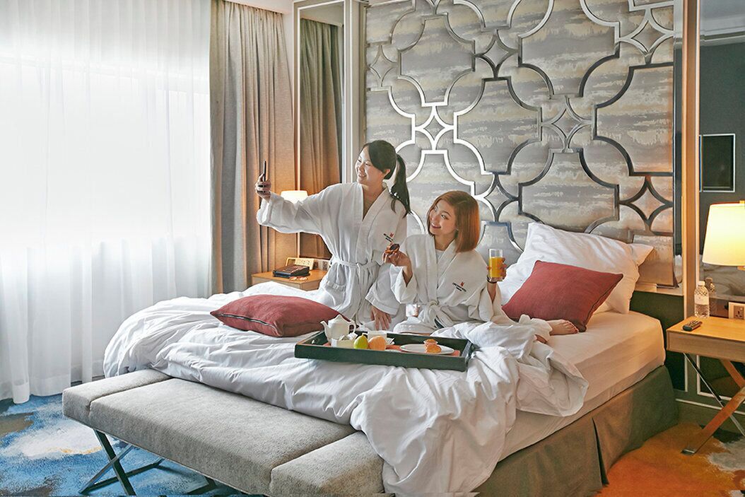 A hotel room with a bed, a bench, and a tray with breakfast items.