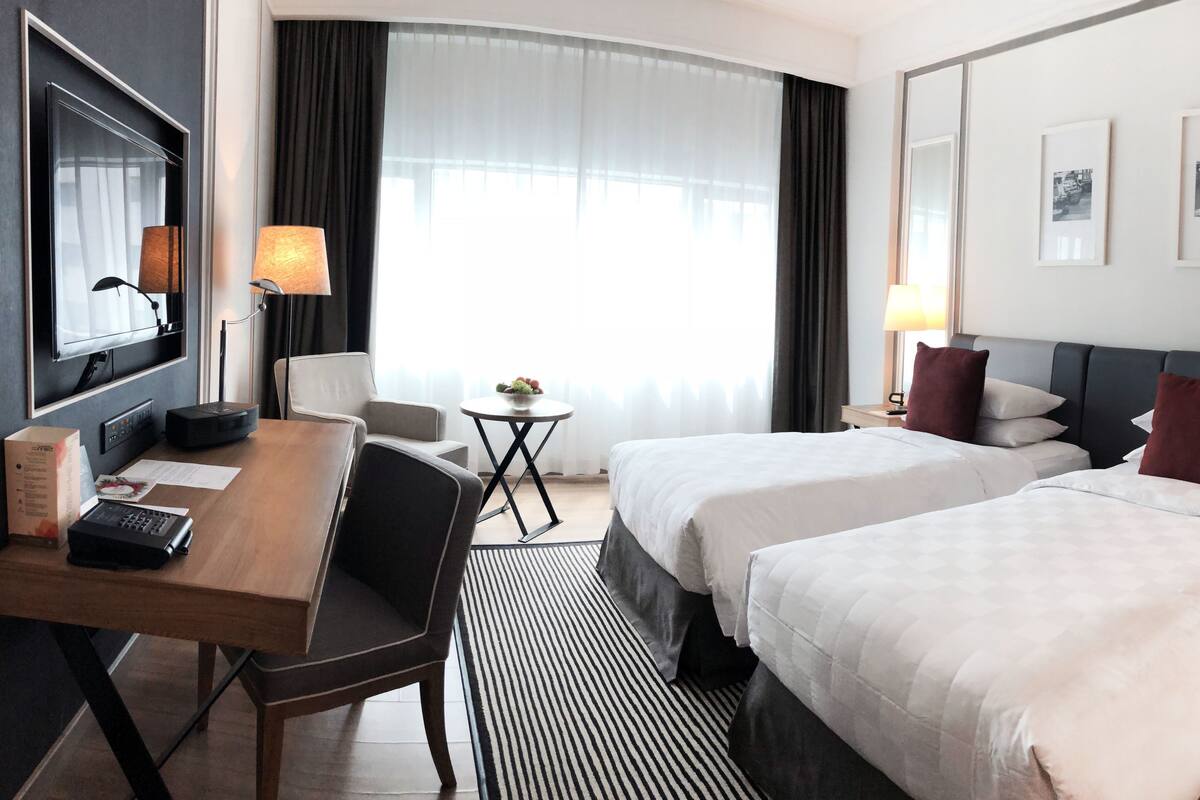 Ein Hotelzimmer mit zwei Betten, einem Schreibtisch, einem Stuhl, einem kleinen Tisch und einer Lampe.