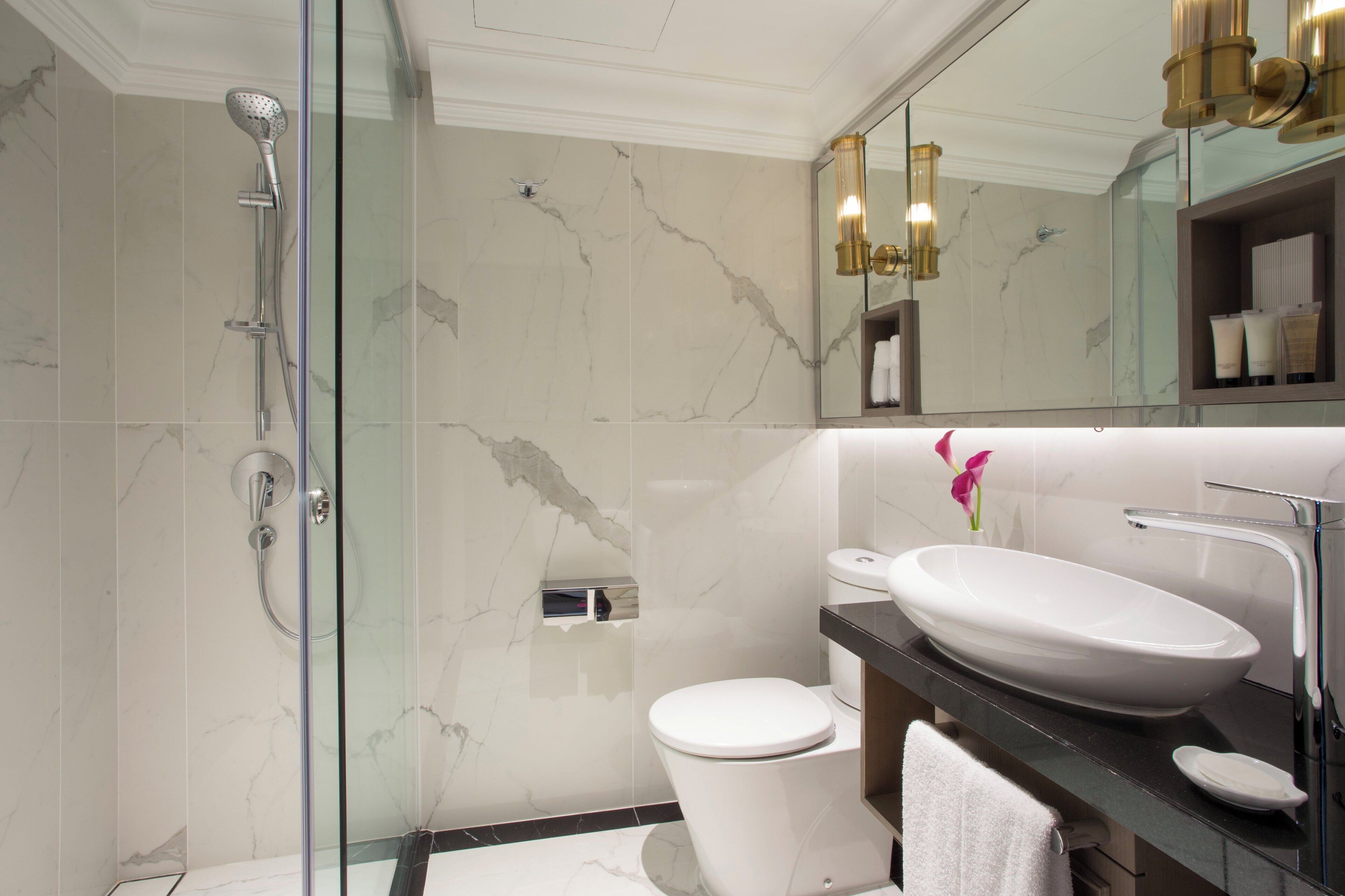 A modern bathroom with a glass-enclosed shower, a white toilet, and a large sink with a mirror above.