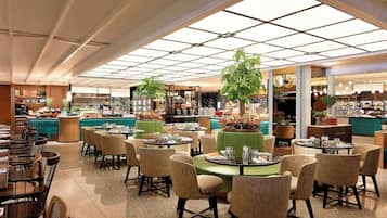 A spacious restaurant with high ceilings, large windows, and a variety of seating arrangements including round tables and booths.