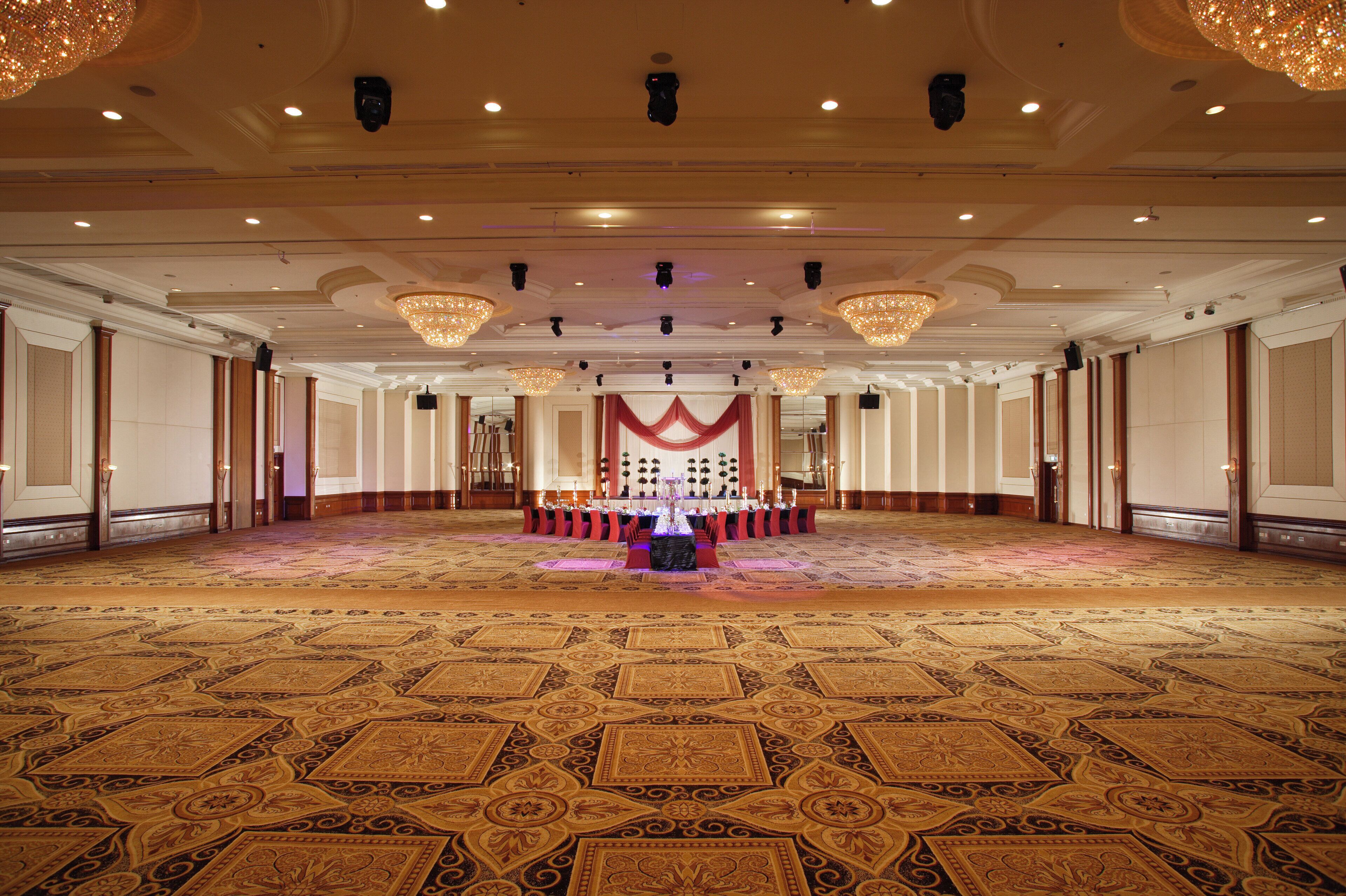 A large, elegantly decorated hall with a patterned carpet, chandeliers, and a central display table.