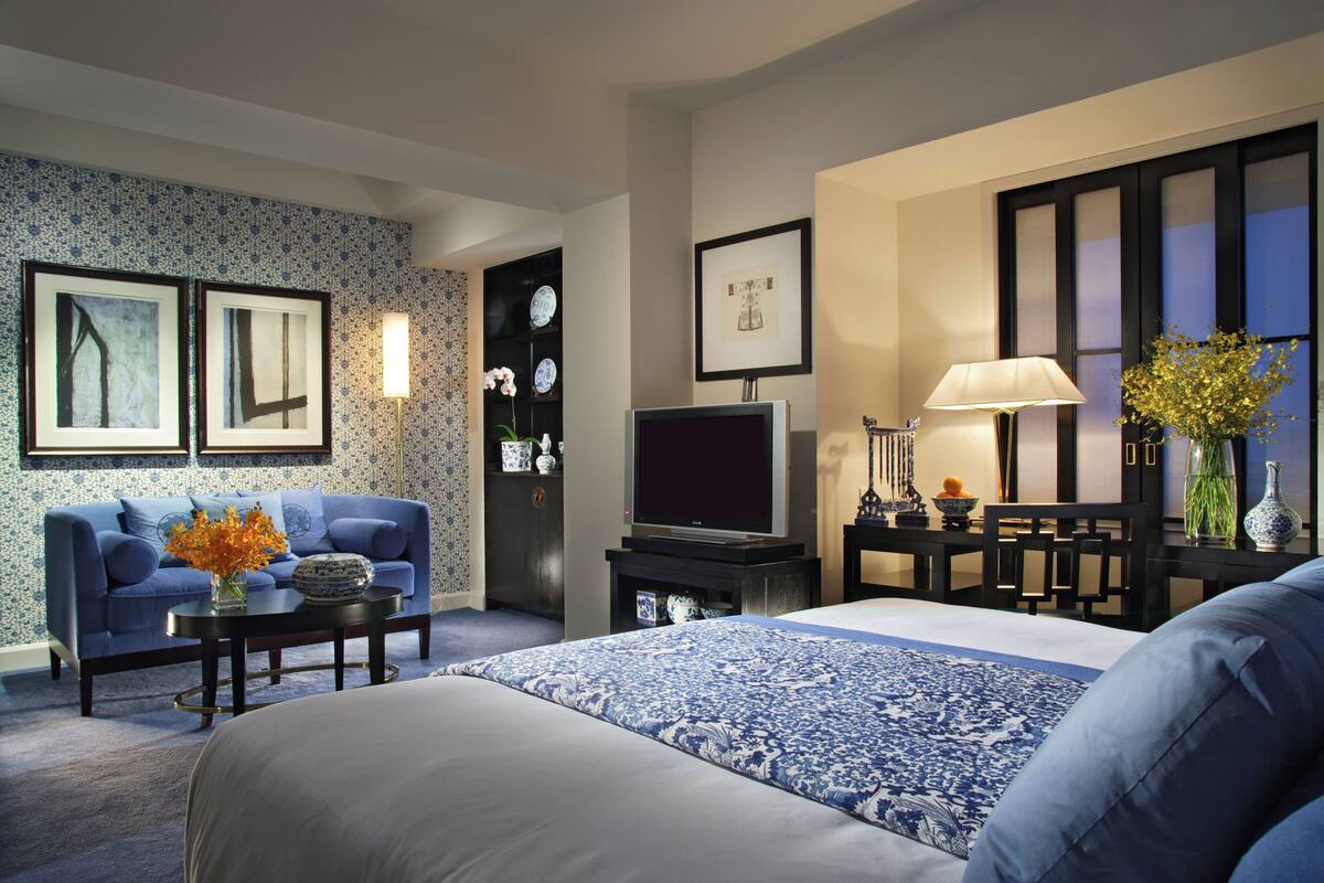 Ein Hotelzimmer mit Bett, Sofa, Fernseher, Lampe und einer Vase mit Blumen.
