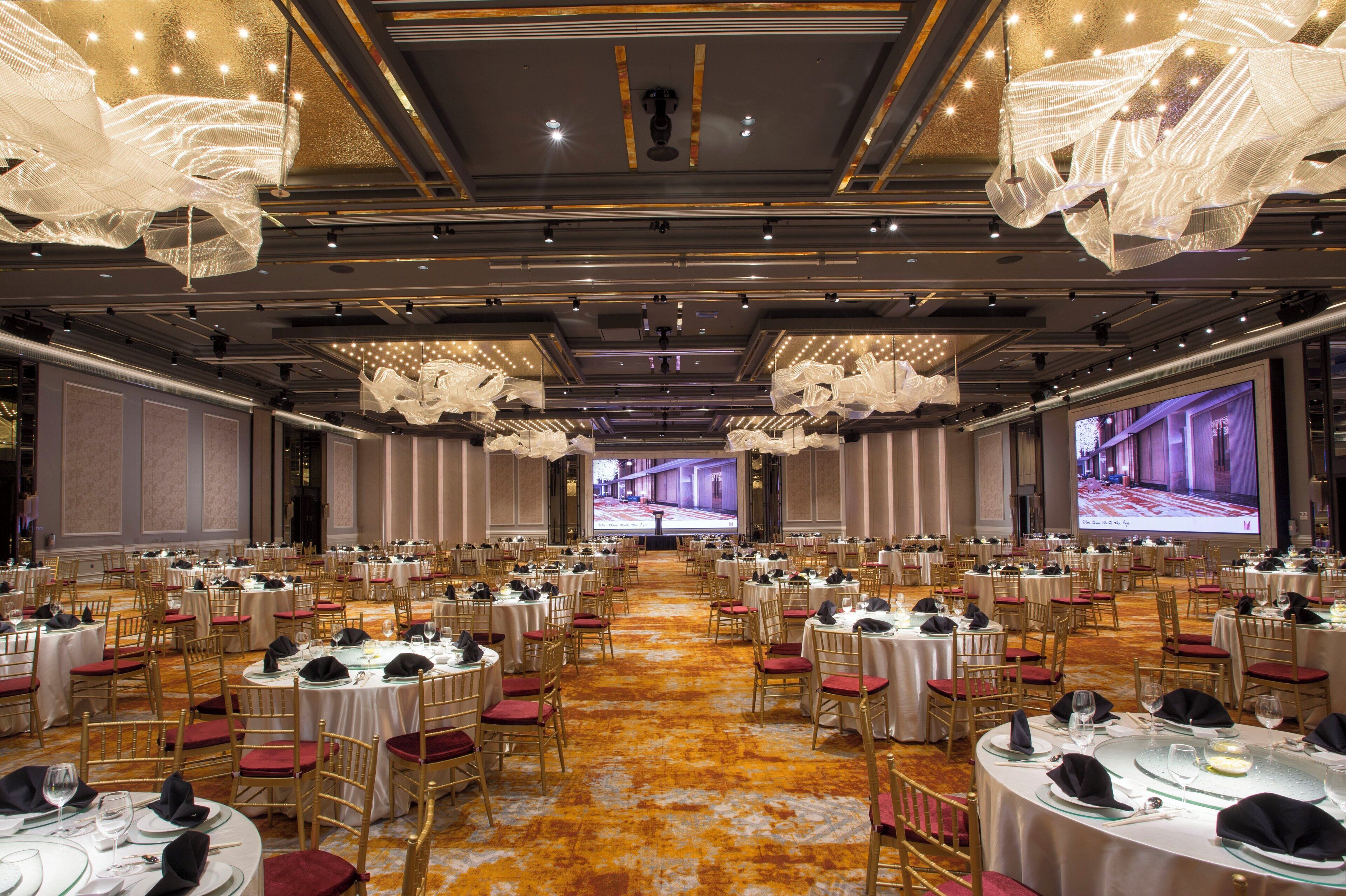Un salón de banquetes con mesas redondas, sillas doradas y suelo alfombrado.
