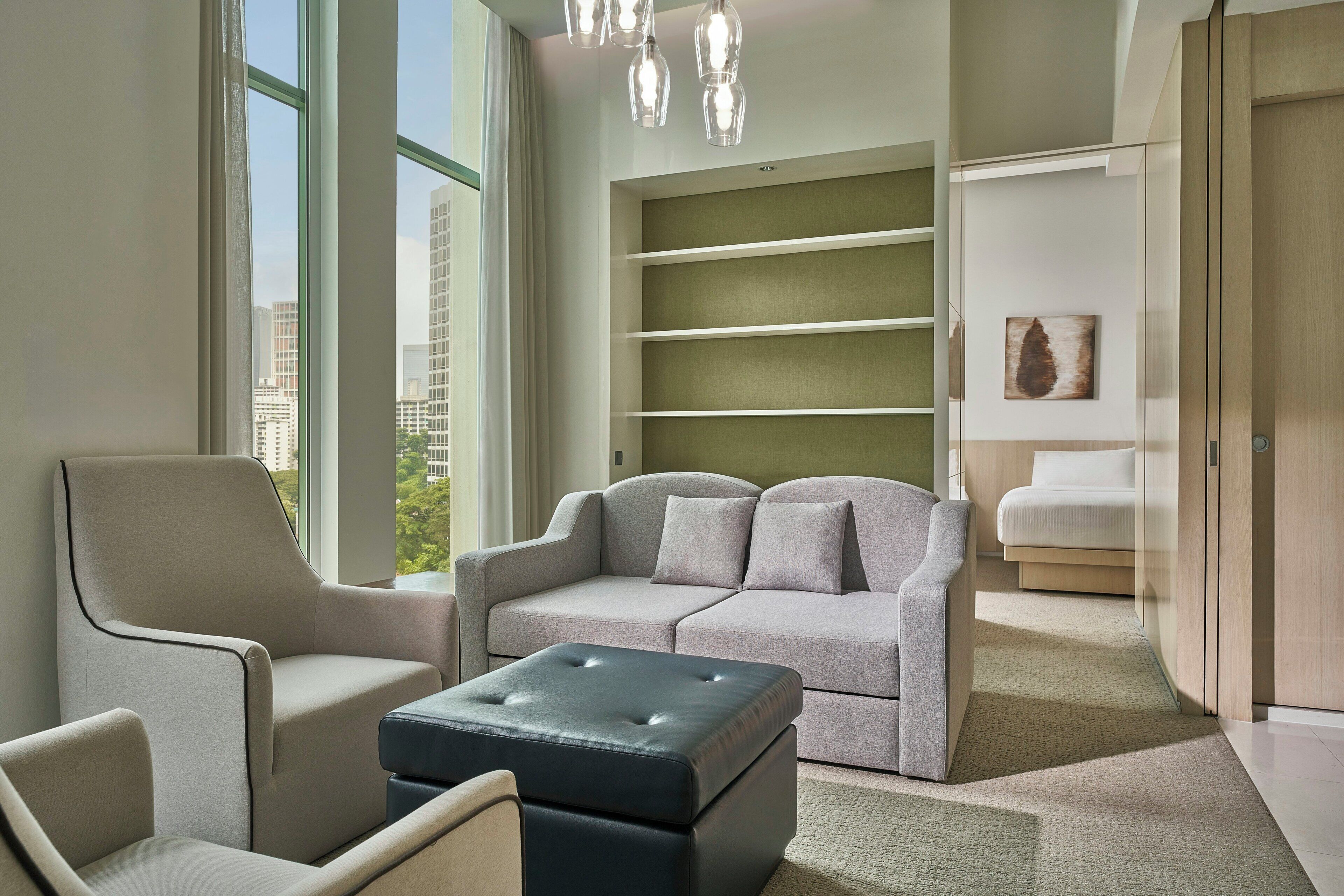 A modern living room with a sofa, armchair, ottoman, and built-in shelves.