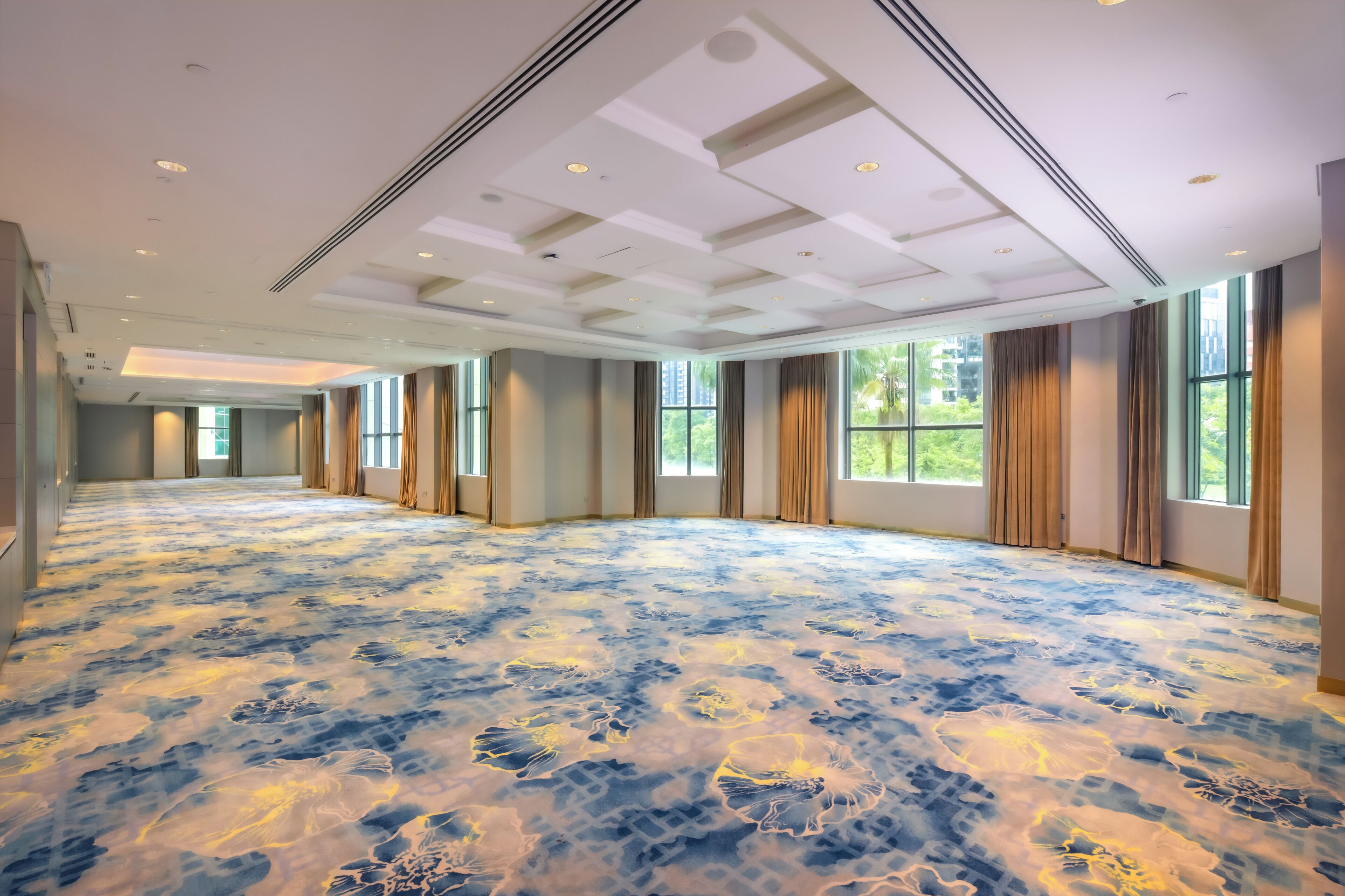 A spacious room with a patterned carpet, large windows, and a high ceiling with recessed lighting.