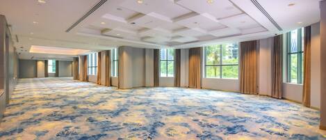 A spacious room with a patterned carpet, large windows, and a high ceiling with recessed lighting.