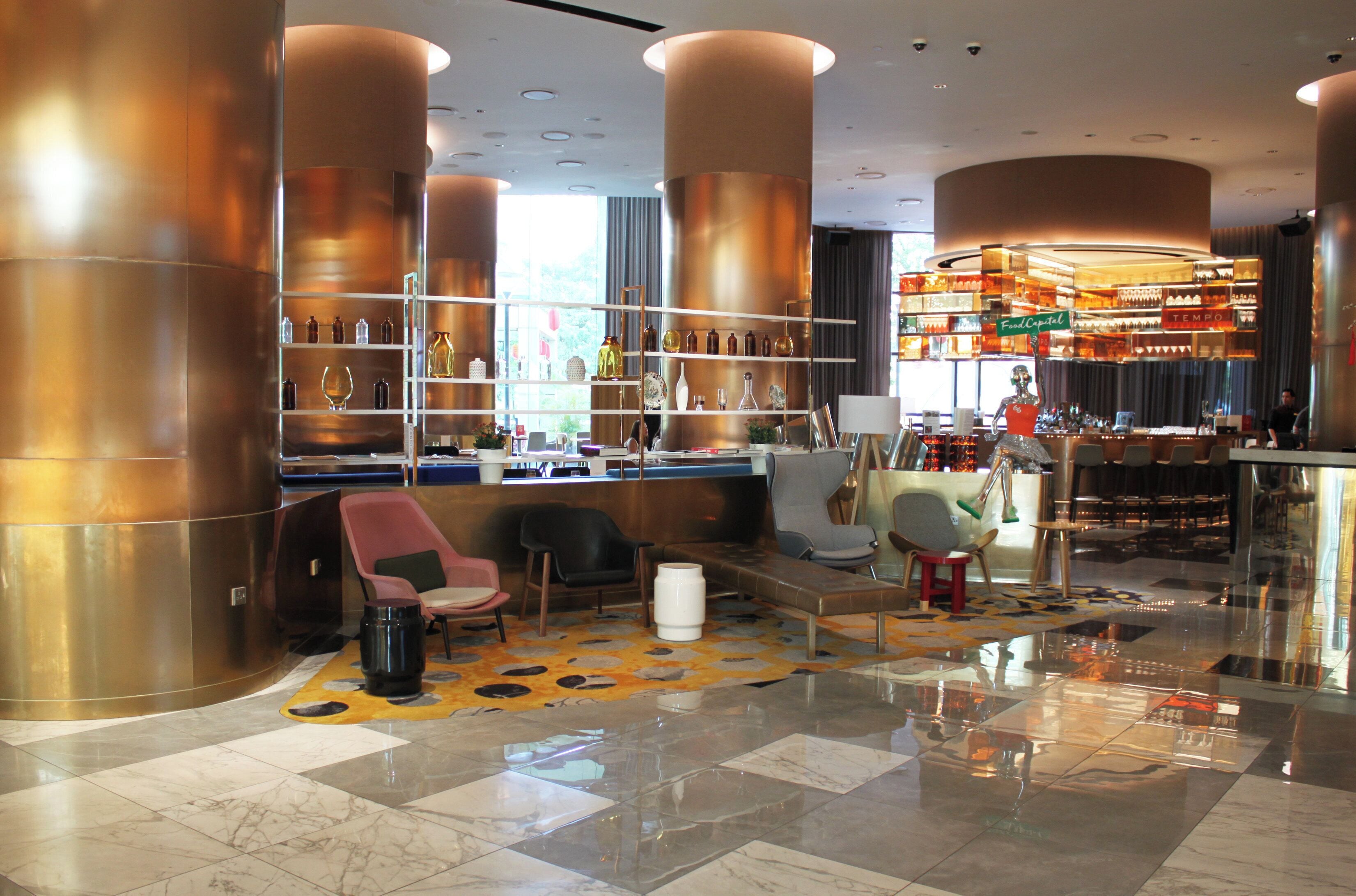 A modern bar area with high ceilings, copper cylindrical columns, and a variety of bar stools.