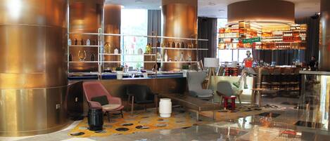 Een moderne bar met hoge plafonds, koperen cilindrische zuilen en diverse barkrukken.