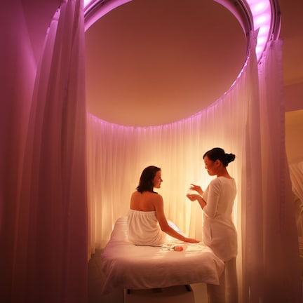 A room with a circular vanity and a bed, featuring a purple ambient light.