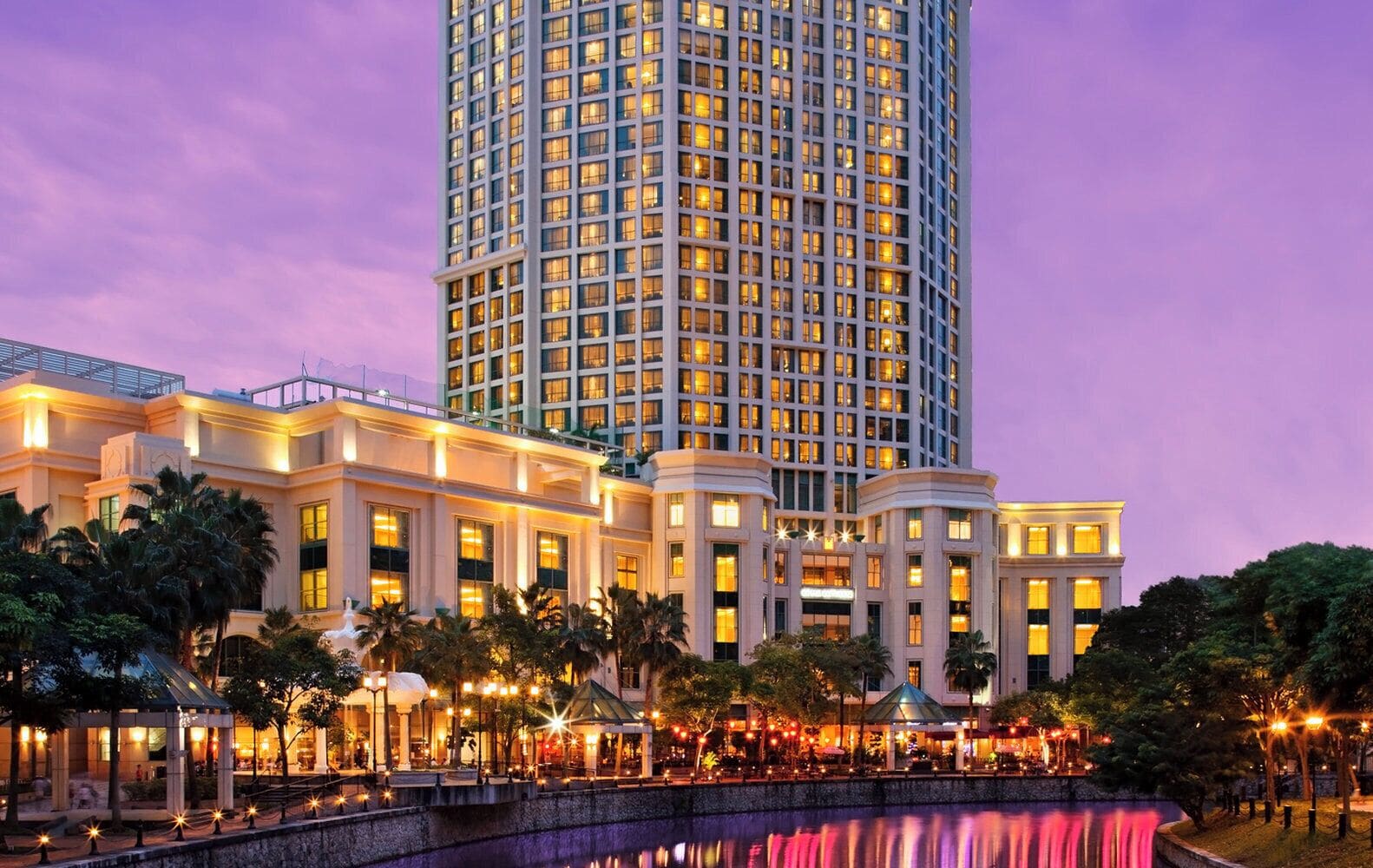 A high-rise hotel with multiple floors, a well-lit facade, and a surrounding landscaped area with palm trees.