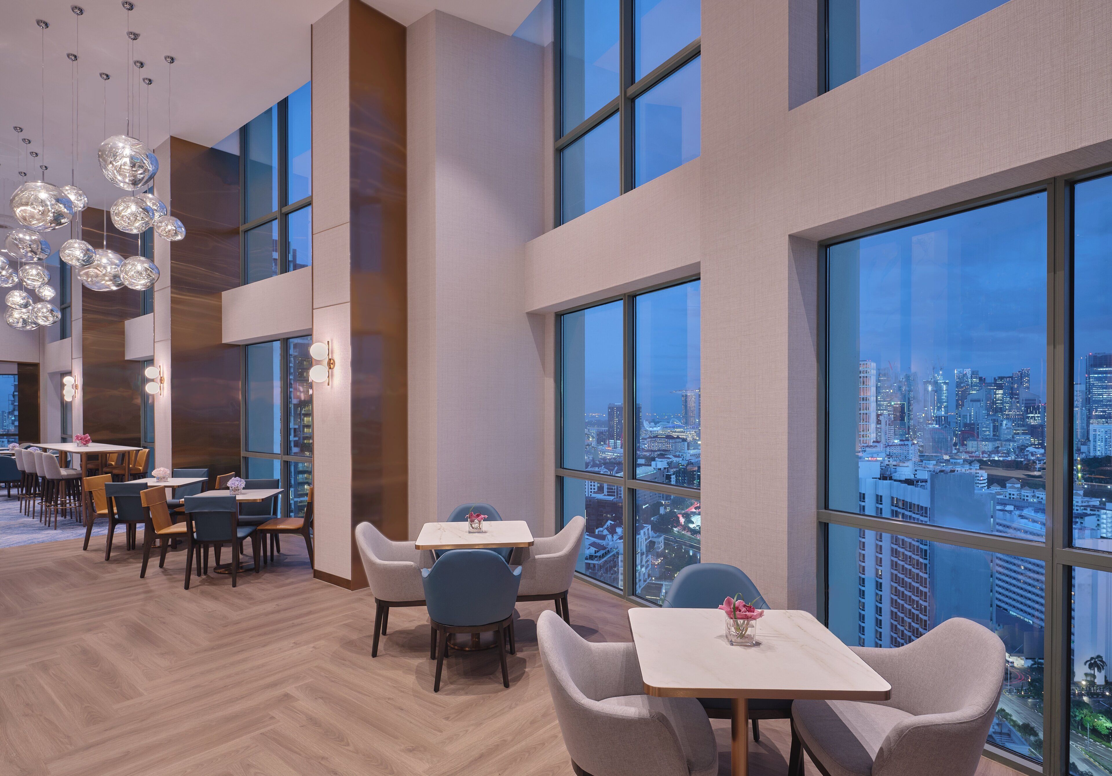 A modern dining area with large windows offering a city view, wooden flooring, and contemporary furniture.
