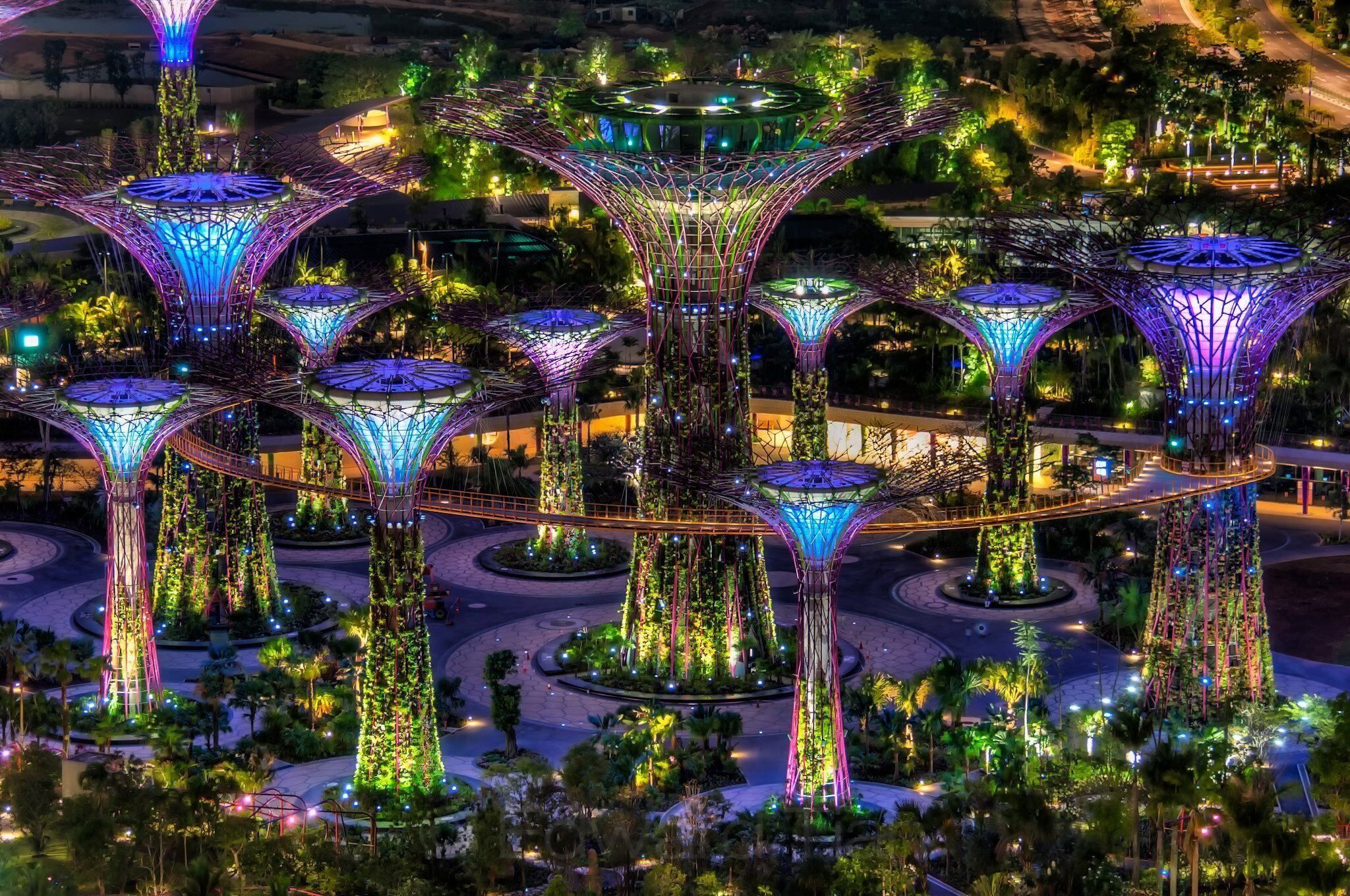 A large, illuminated structure with multiple interconnected towers and a central dome, surrounded by greenery and pathways.