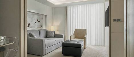 Quarto de hotel moderno com sofá, banquinho, poltrona e televisão de tela plana.