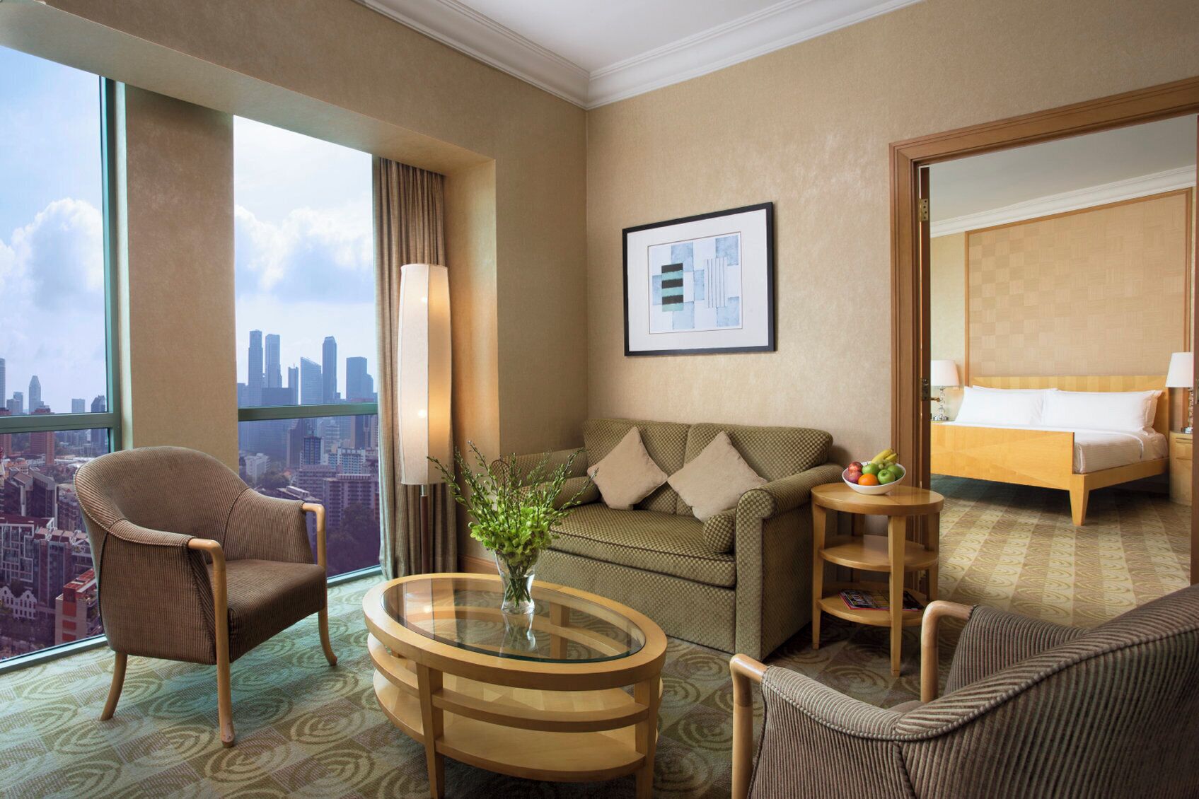 Une chambre d’hôtel avec une grande fenêtre, un canapé, un fauteuil, une table ronde et un lit.