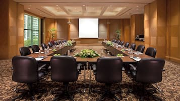 A conference room with a long table, multiple chairs, and a projector screen.