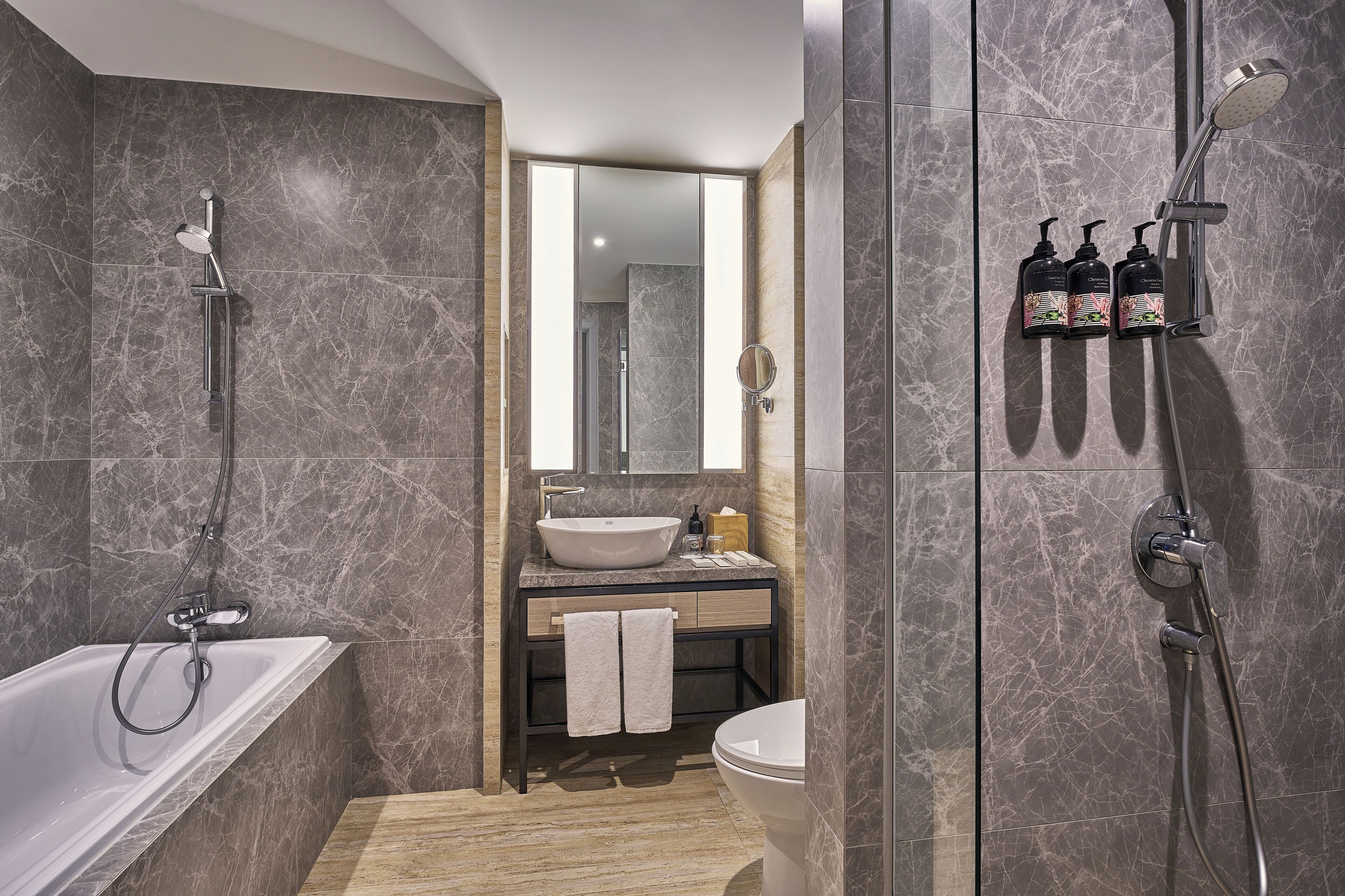 A modern bathroom with a bathtub, a sink, and a shower. There are two towels hanging on the sink area.