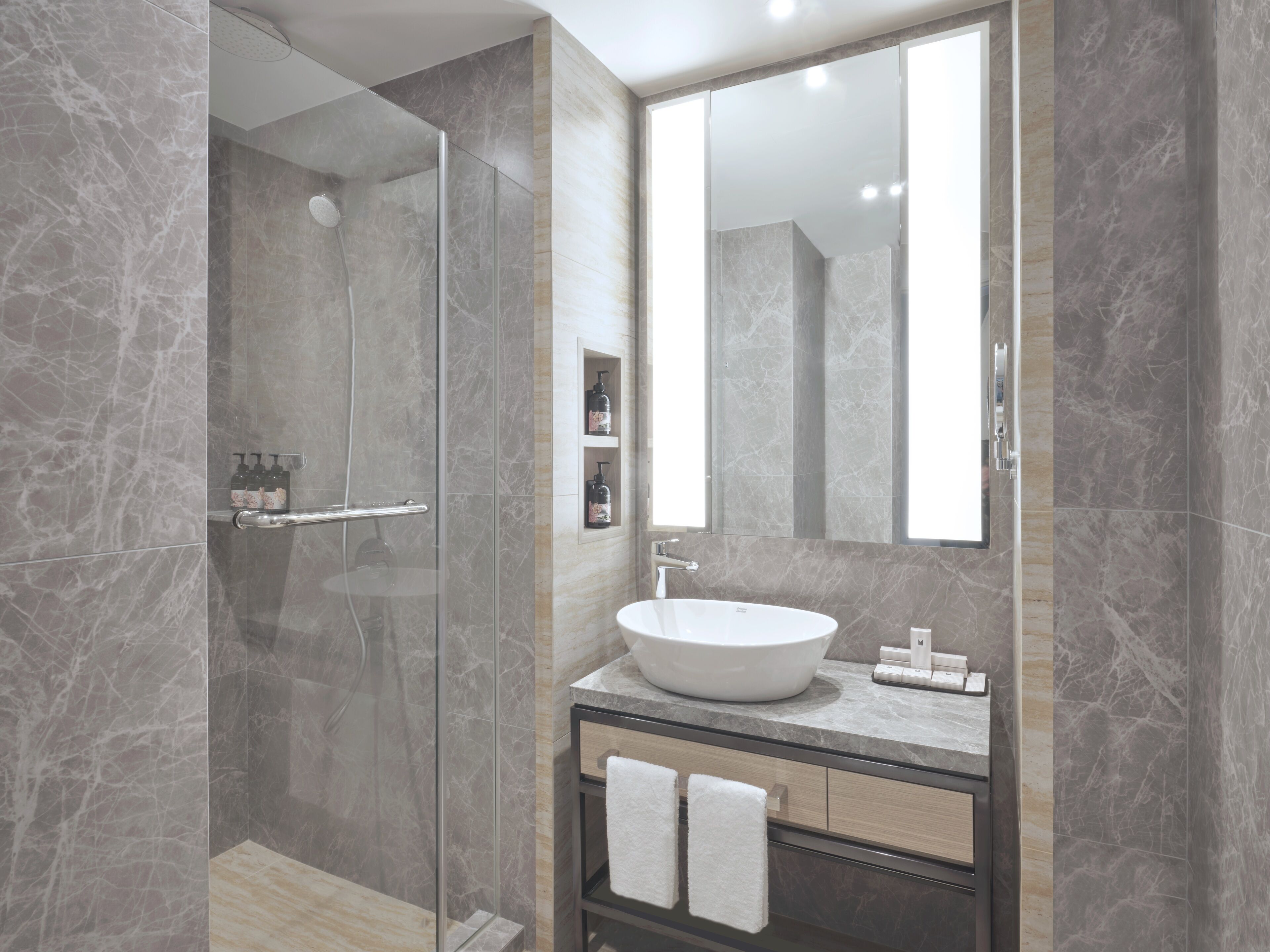 Un baño moderno con ducha acristalada, un espejo grande y un tocador con lavabo y toallero.