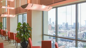 A spacious lobby with large windows offering a city view, modern pendant lighting, and red upholstered chairs.