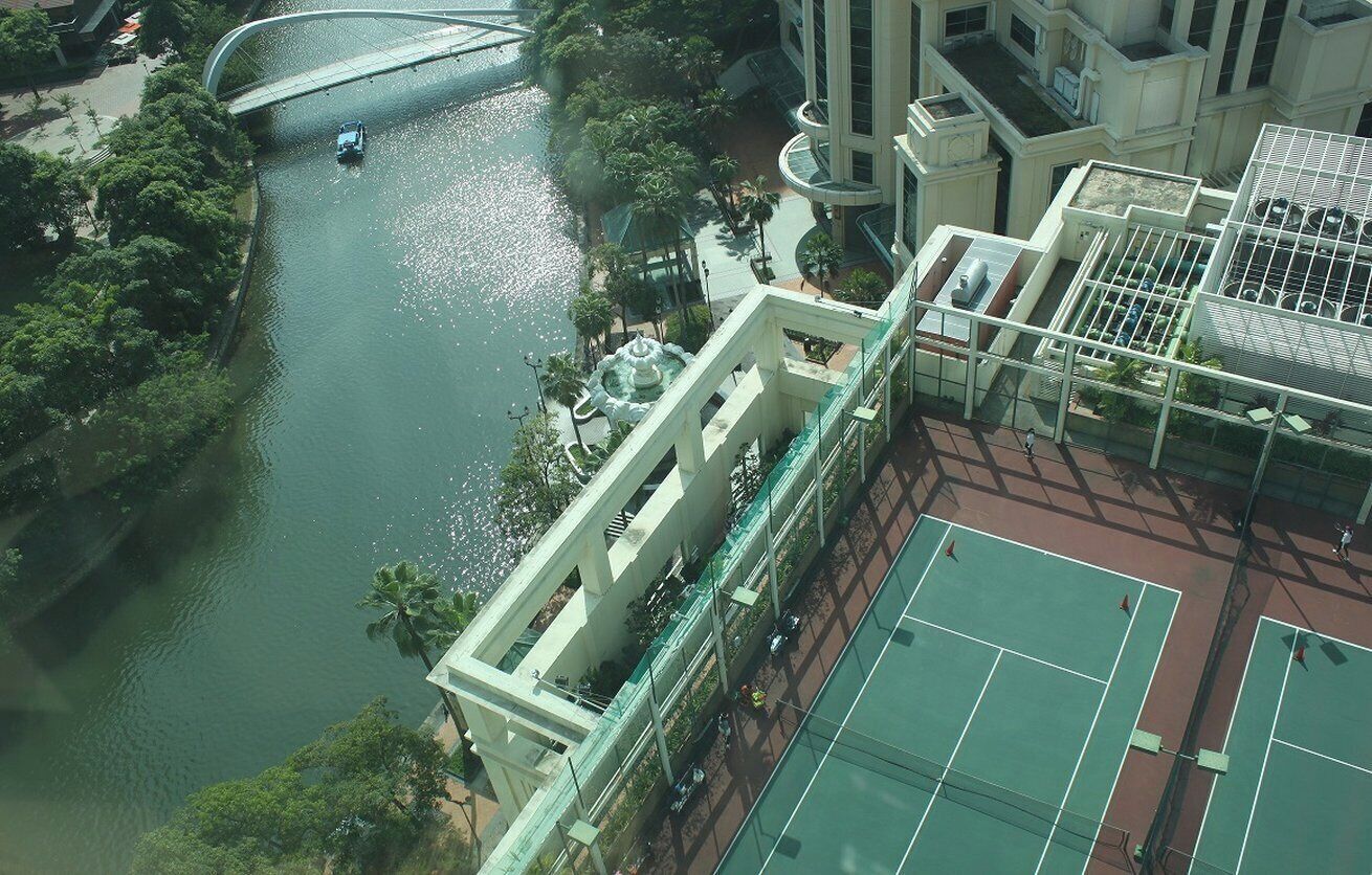 Un edificio de gran altura con cancha de tenis, un río y un puente.