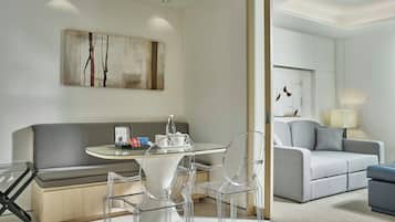 A modern living room with a sofa, a glass dining table, clear chairs, and a painting on the wall.