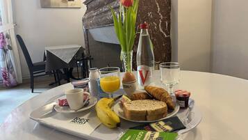 A breakfast tray with bread, croissants, a banana, a croissant, a glass of orange juice, a bottle of water, a glass of milk, a cup, a small container of jam, and a package of Gouda cheese.