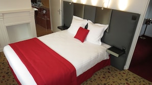 A hotel room with a bed, a nightstand, a bedside table, a mirror, and a bathroom with a toilet and sink. - Belle Hôtel, Lille Ouest (Bailleul)