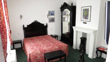 A bedroom with a large bed, a small bedside table, a mirror, and a fireplace.