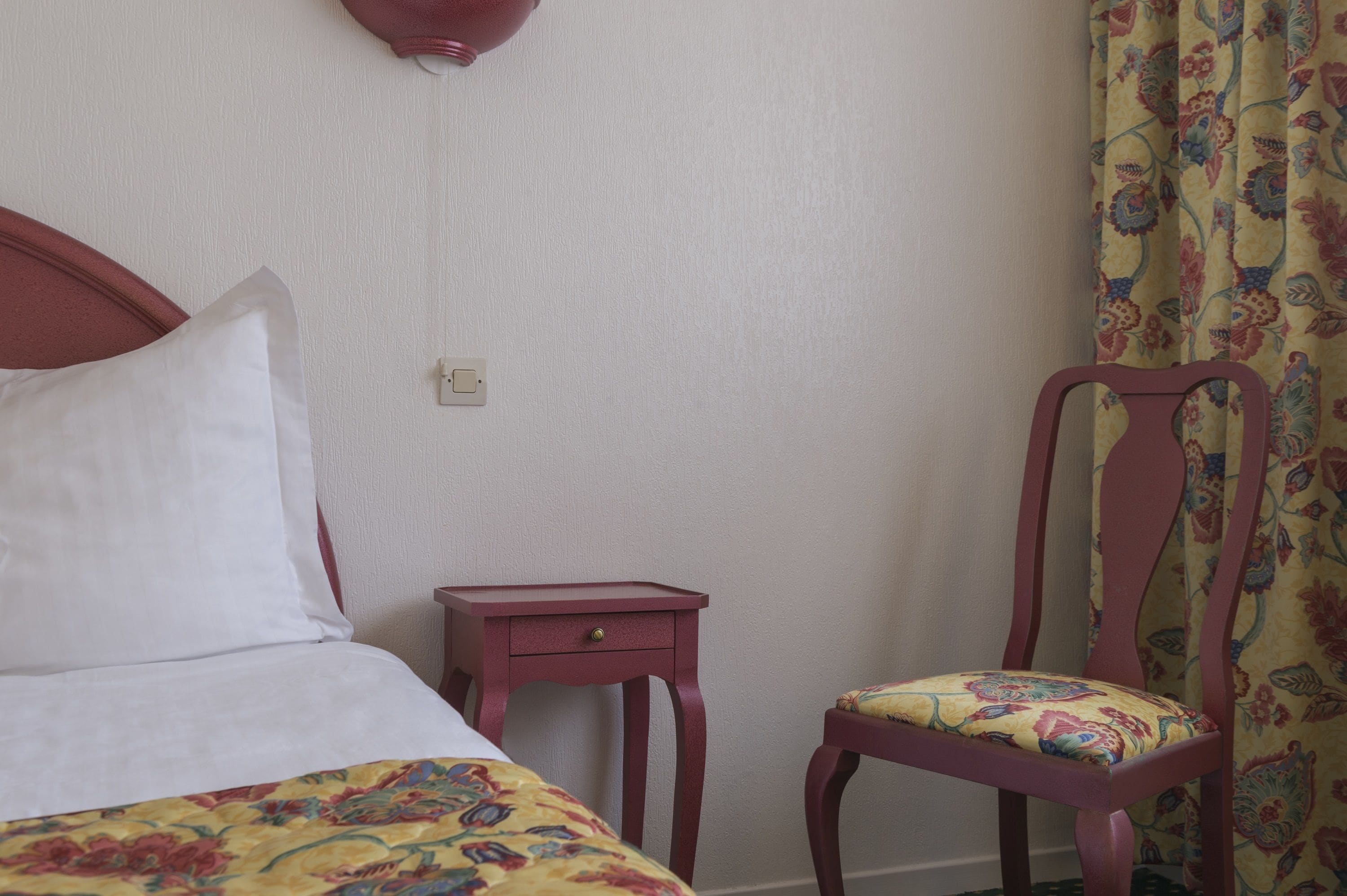 Une chambre à coucher comprenant un lit, une table de chevet, une chaise et une lampe fixée au mur.