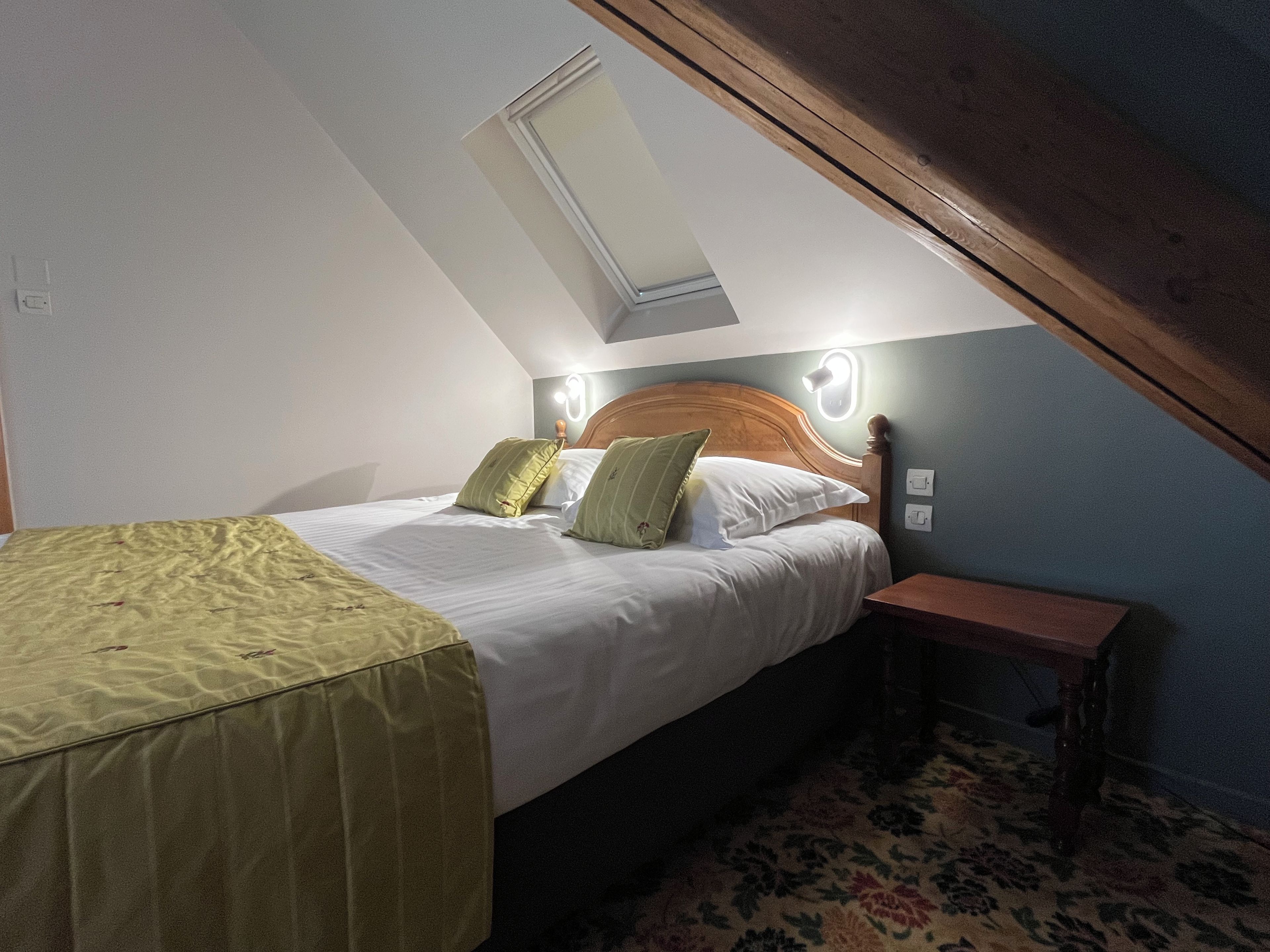 A bedroom with a sloped ceiling, a bed with pillows, a bedside table, and a wall-mounted light fixture.