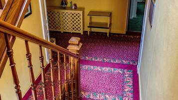 A staircase with a patterned carpet leading to a room with a chandelier and framed pictures on the wall.