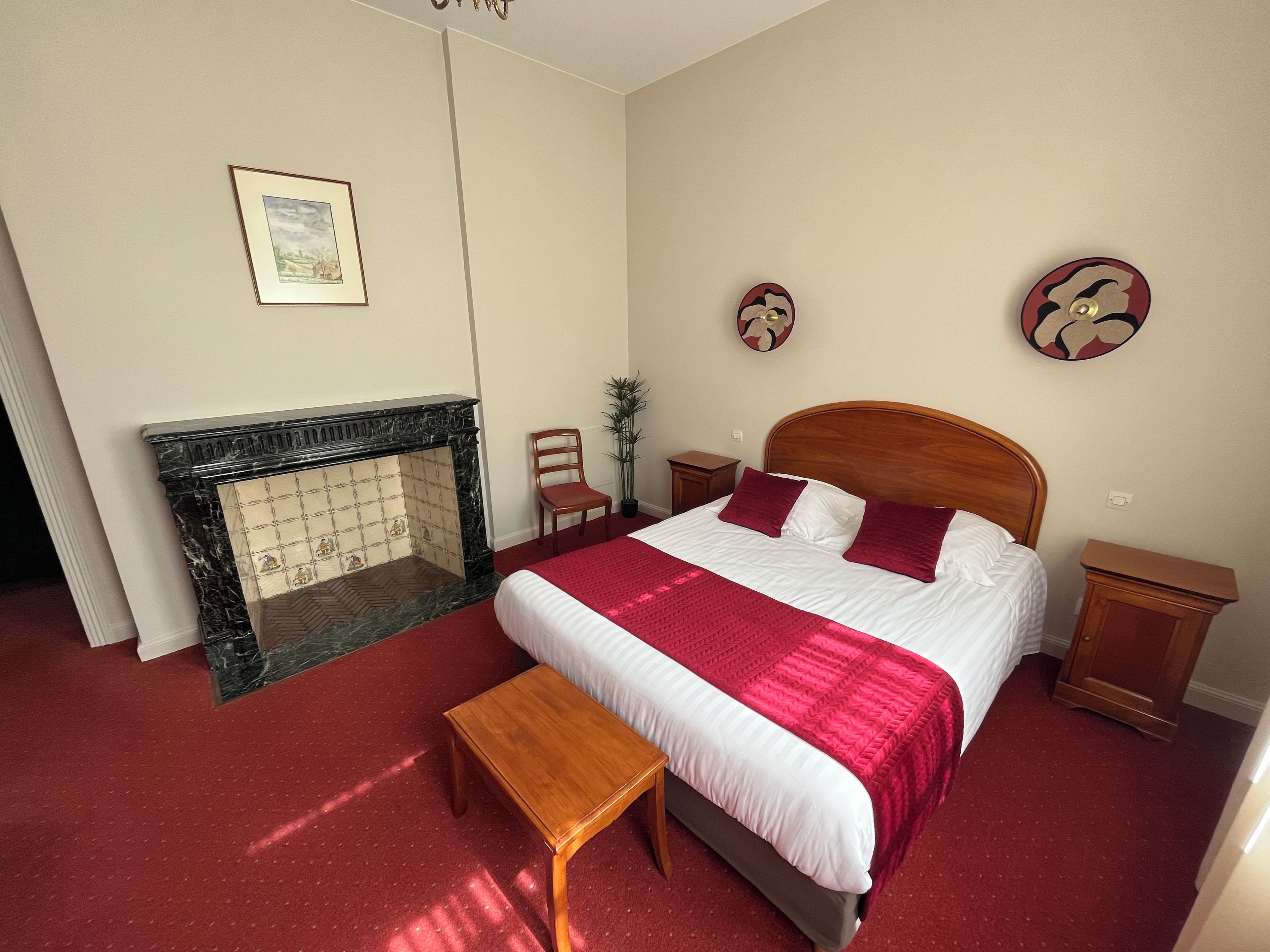 A hotel room with a bed, a wooden headboard, a fireplace, a small table, and two nightstands.