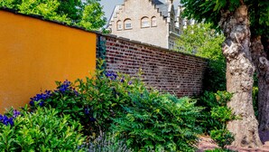 A garden with a brick wall, various plants, and a large tree. - Belle Hôtel, Lille Ouest (Bailleul)
