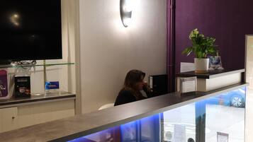 A reception desk with a flat-screen TV, a potted plant, and a glass counter.