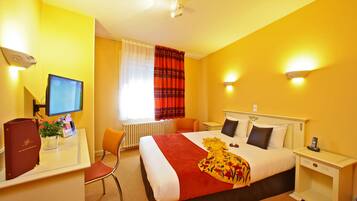 Une chambre d’hôtel avec un lit, un bureau avec un ordinateur, une chaise et une fenêtre avec des rideaux.