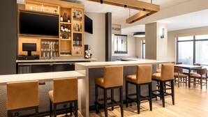 Eine moderne Bar mit einer langen Theke, verschiedenen Sitzgelegenheiten und einer Auswahl an Flaschen und Gläsern.