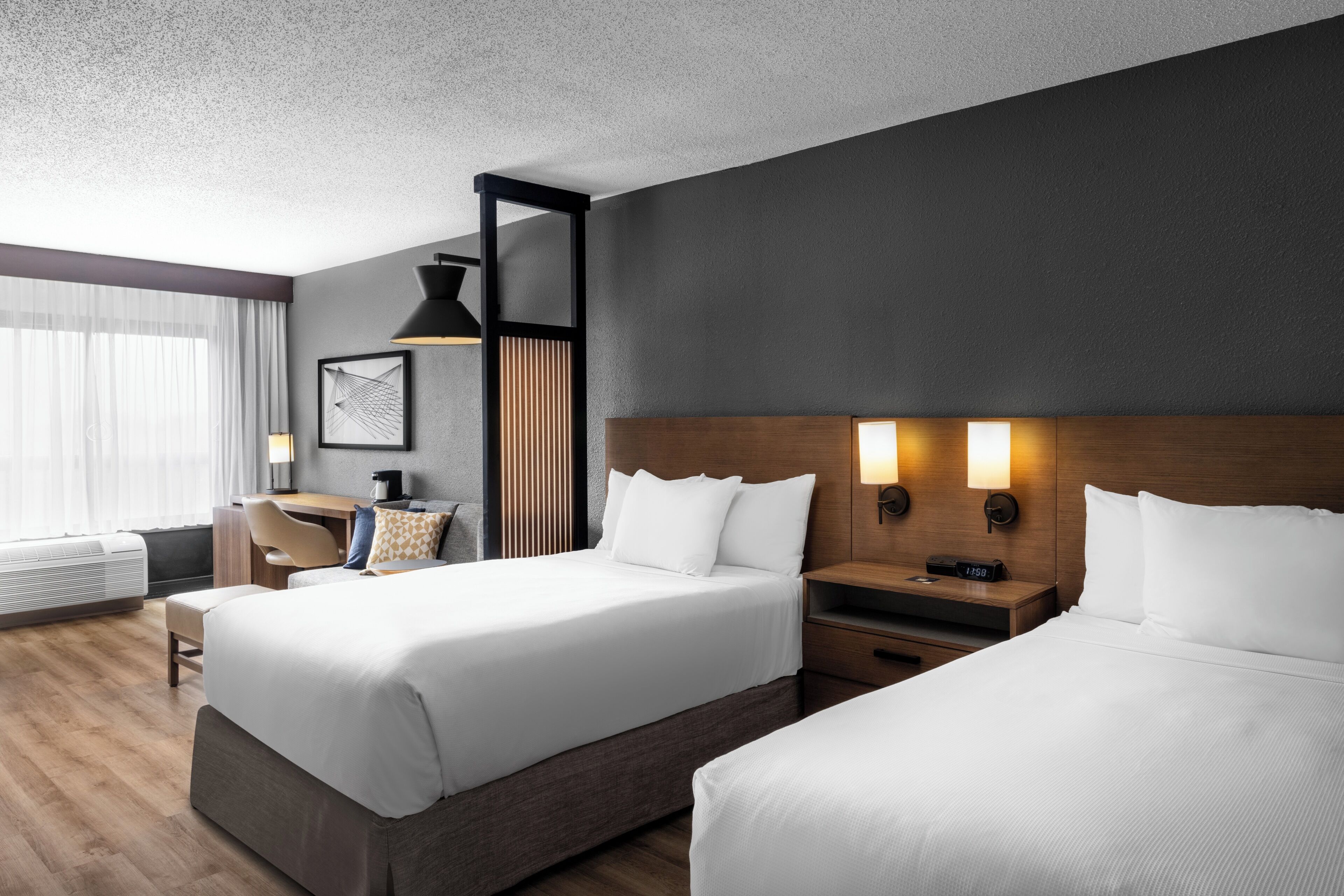 A hotel room with two beds, a desk, a chair, a coffee maker, and a clock.