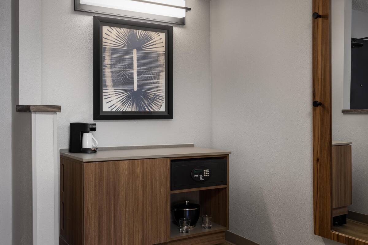 Ein modernes Badezimmer mit einem Holzschrank, einem gerahmten Kunstwerk und einer Kaffeemaschine.