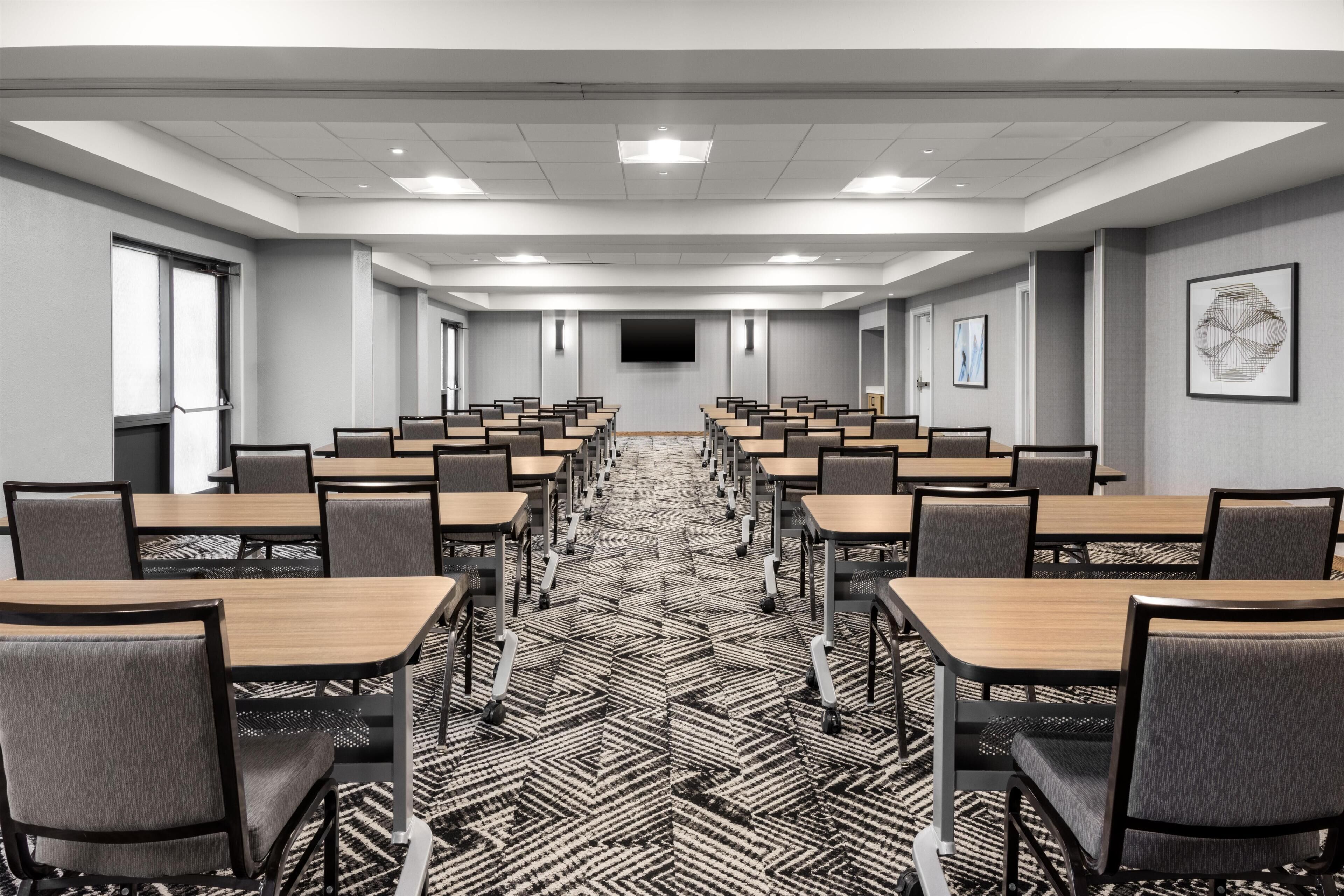 A conference room with rows of tables and chairs, a flat-screen TV, and a patterned carpet.