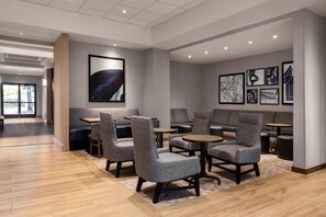 Un espace de détente moderne avec des fauteuils et des tables aux revêtements gris, des œuvres d’art encadrées accrochées aux murs et un plancher en bois.