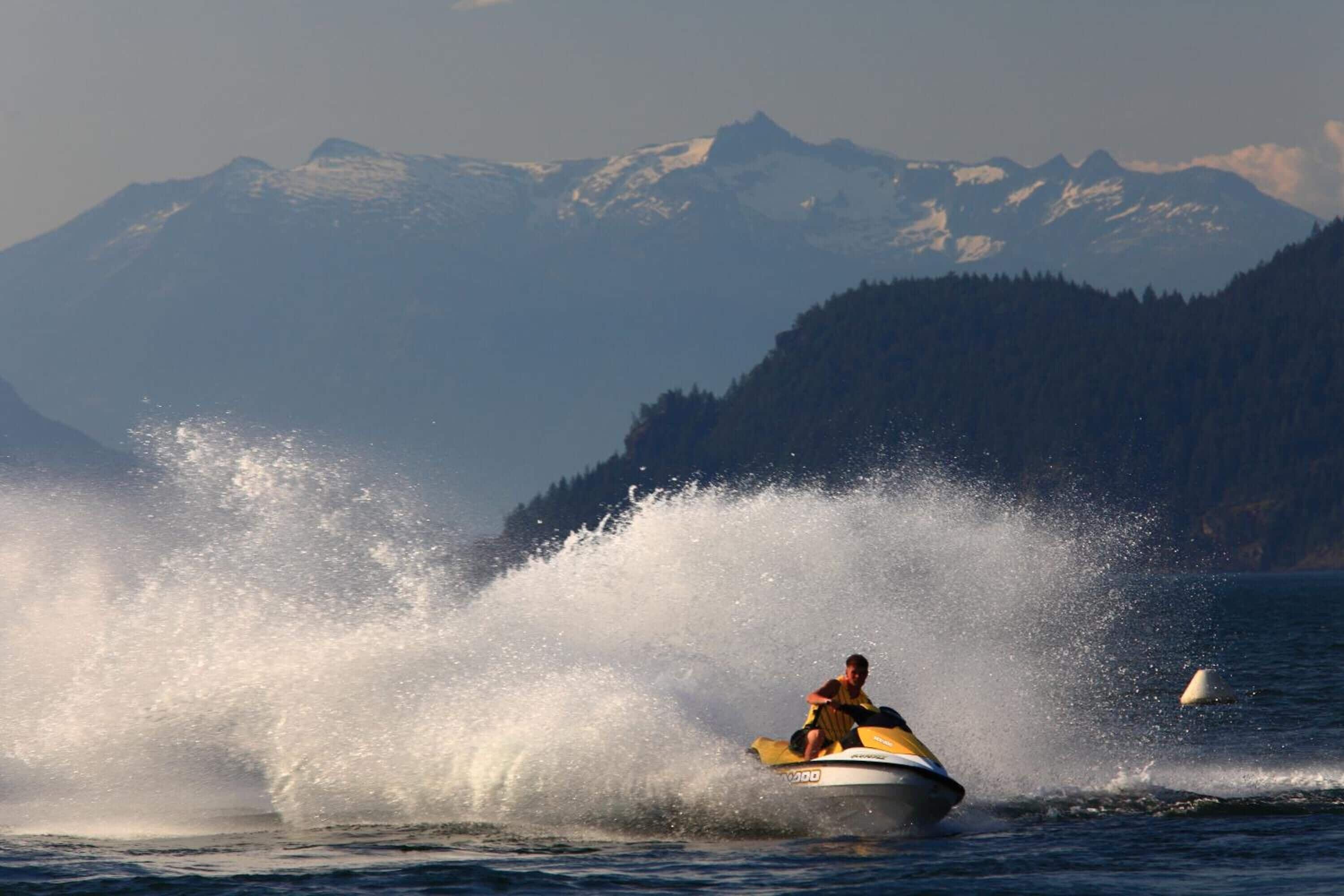 A person jet-skiing on a body of water with a mountainous landscape in the background.