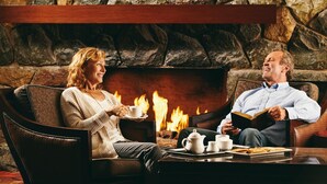 A couple seated in leather armchairs by a fireplace with a stone wall backdrop. - Harrison Hot Springs Resort and Spa (Harrison Hot Springs)