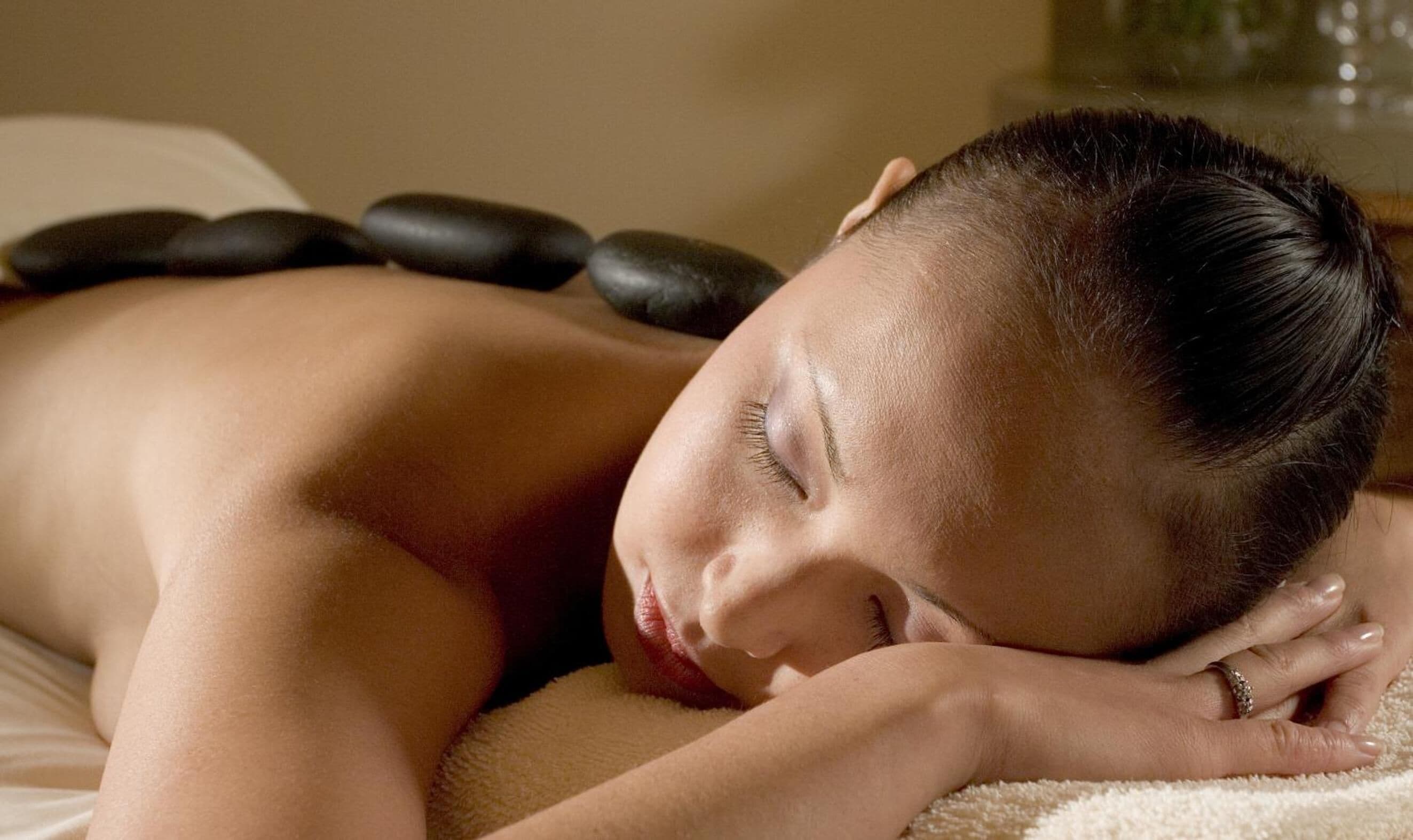 A person lying on a massage table with stones placed on their back.