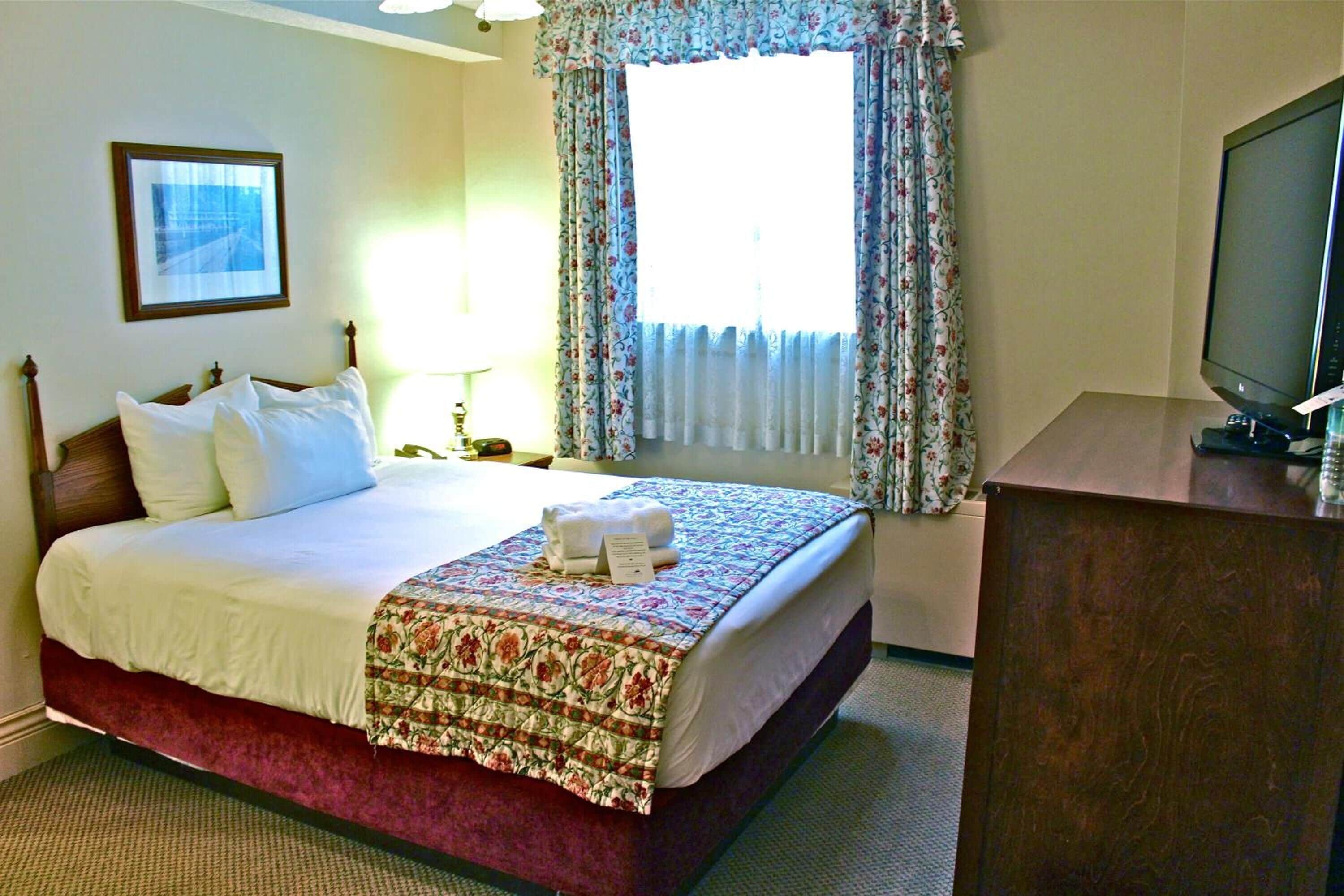 A hotel room with a bed, a desk, a television, and a window with curtains.