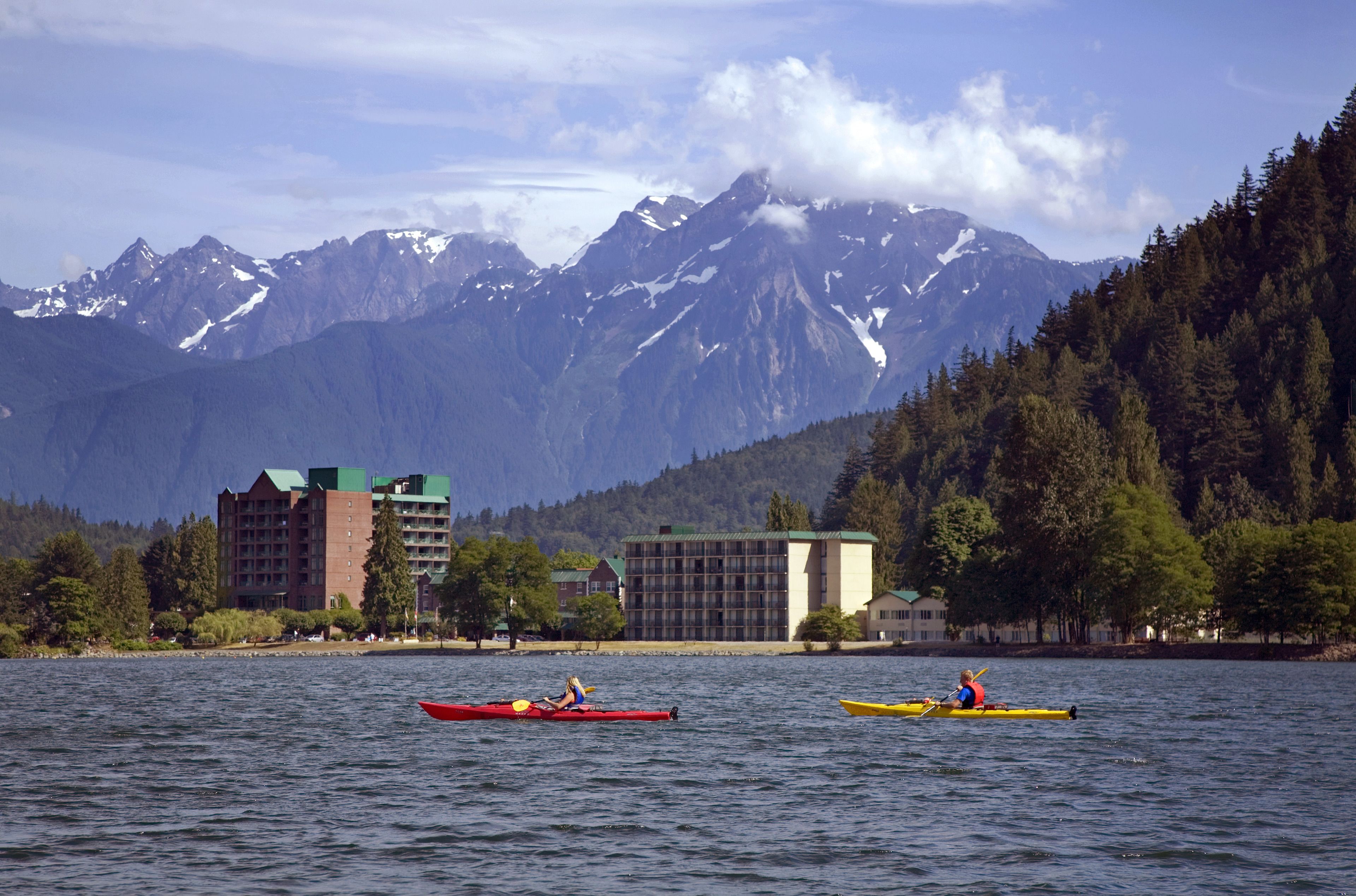 A lake with kayaks, buildings, and mountains in the background.