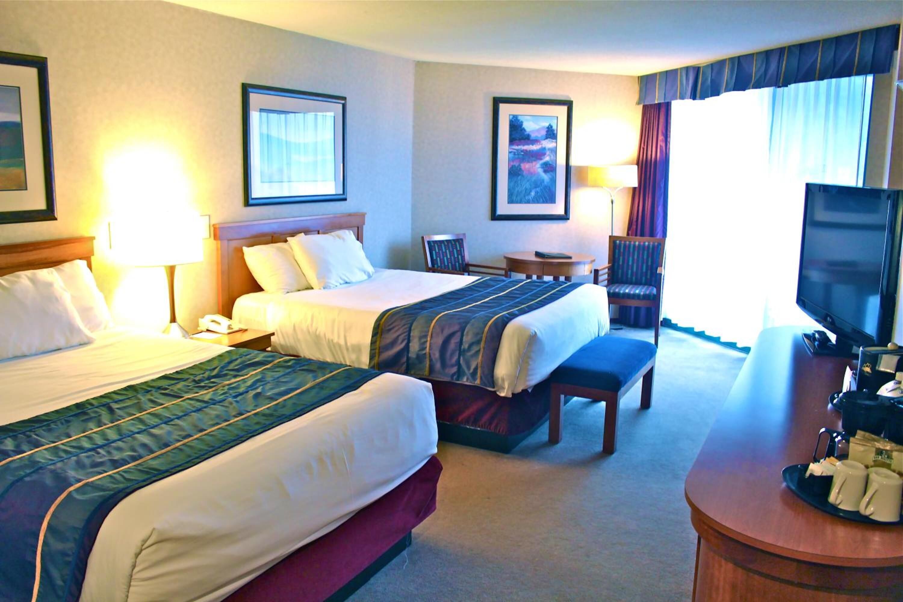 A hotel room with two beds, a desk with a TV, and a chair.