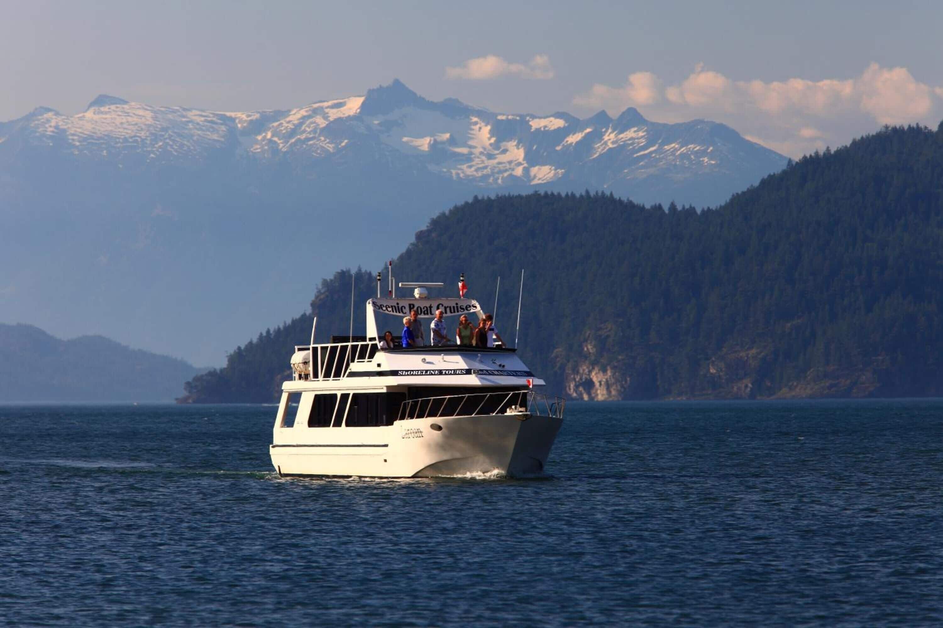 Un bateau portant l’inscription « Scenic Boat Cruises » sur le côté, naviguant sur l’eau avec des montagnes en arrière-plan.