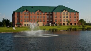 A multi-story hotel with a green roof, a fountain in front, and a grassy area beside a body of water. - Staybridge Suites West Des Moines by IHG (West Des Moines)