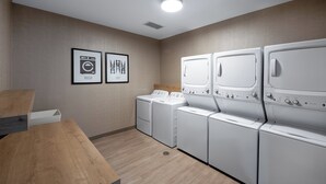 A laundry room with four white washers and dryers, wooden flooring, and two framed signs indicating wash and dry cycles. - Staybridge Suites West Des Moines by IHG (West Des Moines)