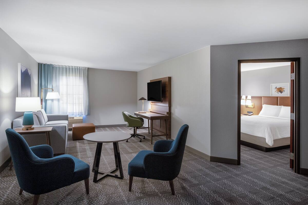 A hotel room with a bed, a desk, two chairs, a small table, and a window with curtains.