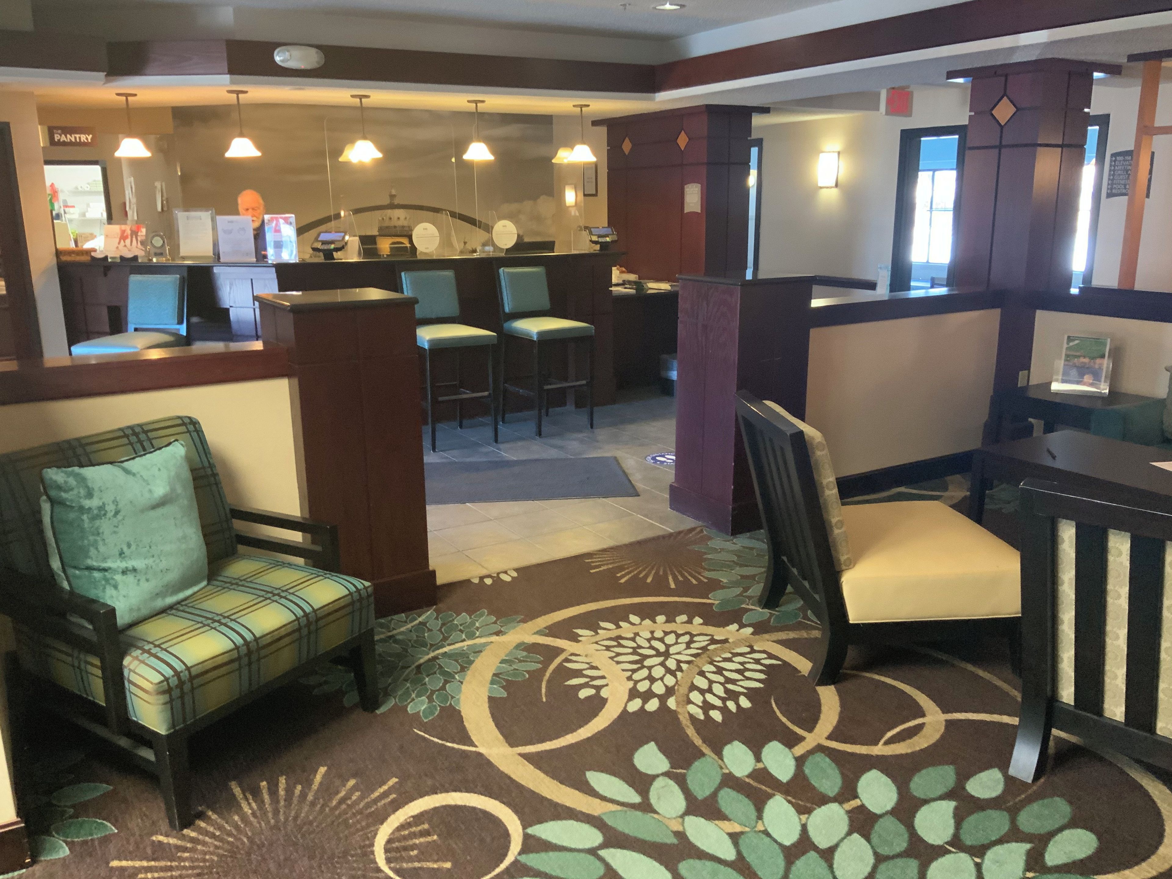 Un vestíbulo de hotel con mostrador de recepción, zona de estar y alfombra estampada.